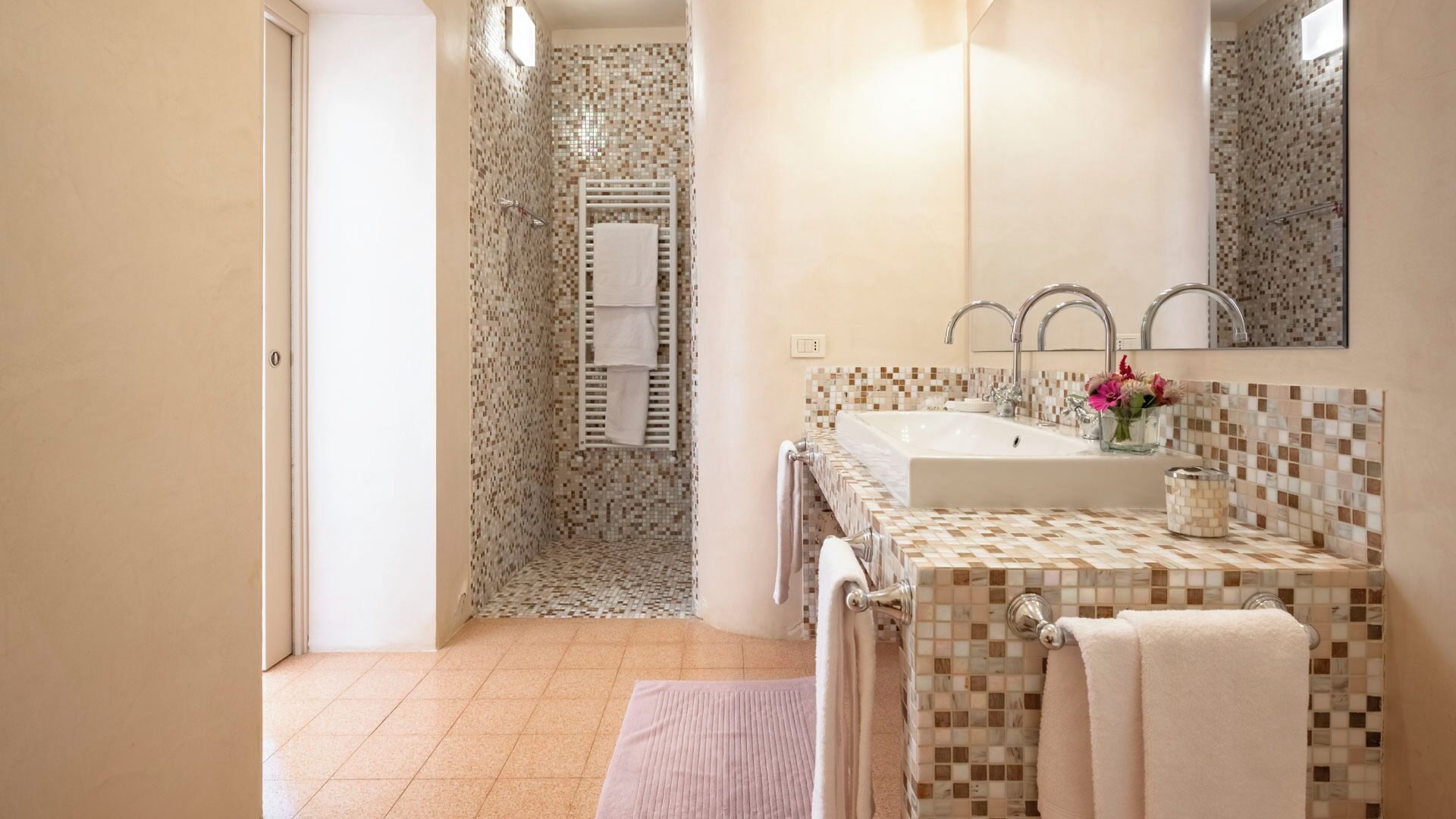 Une salle de bain avec une douche carrelée, un lavabo avec un miroir et un porte-serviettes.