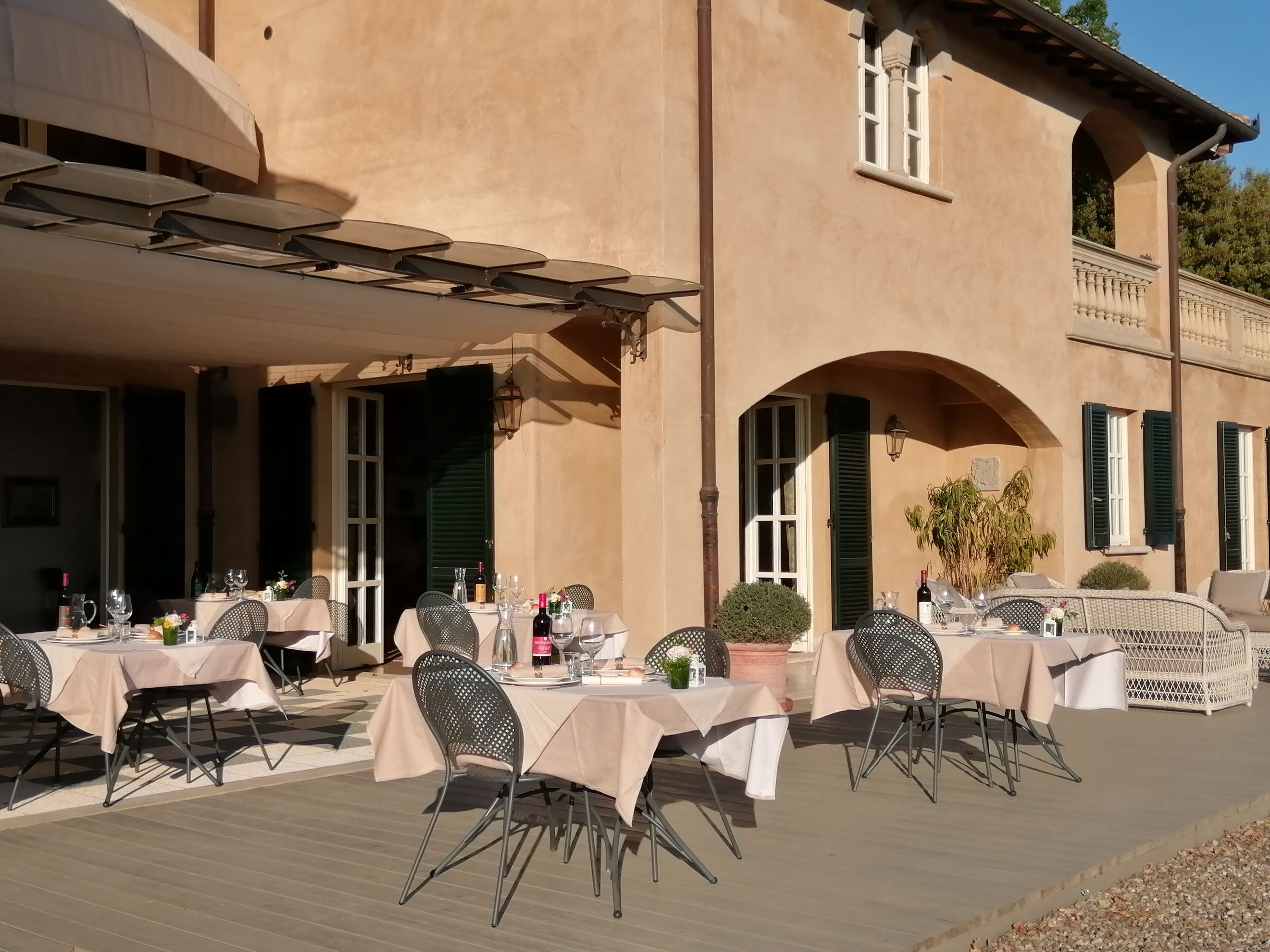 An outdoor dining area with tables and chairs, a covered section, and a building with arches and windows.