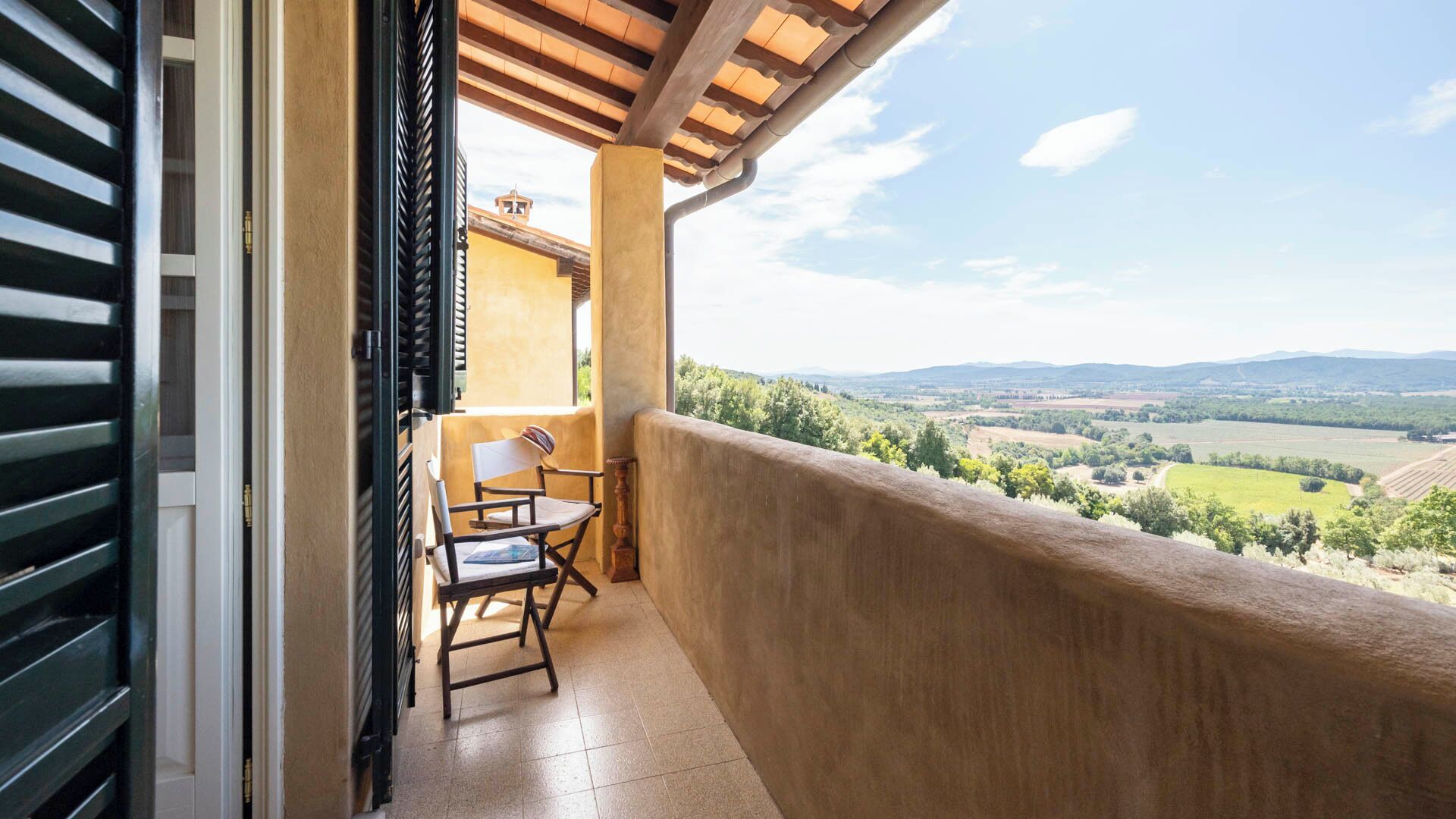 Un balcón con mesa y sillas, con vistas a un paisaje pintoresco con campos y colinas al lejano.