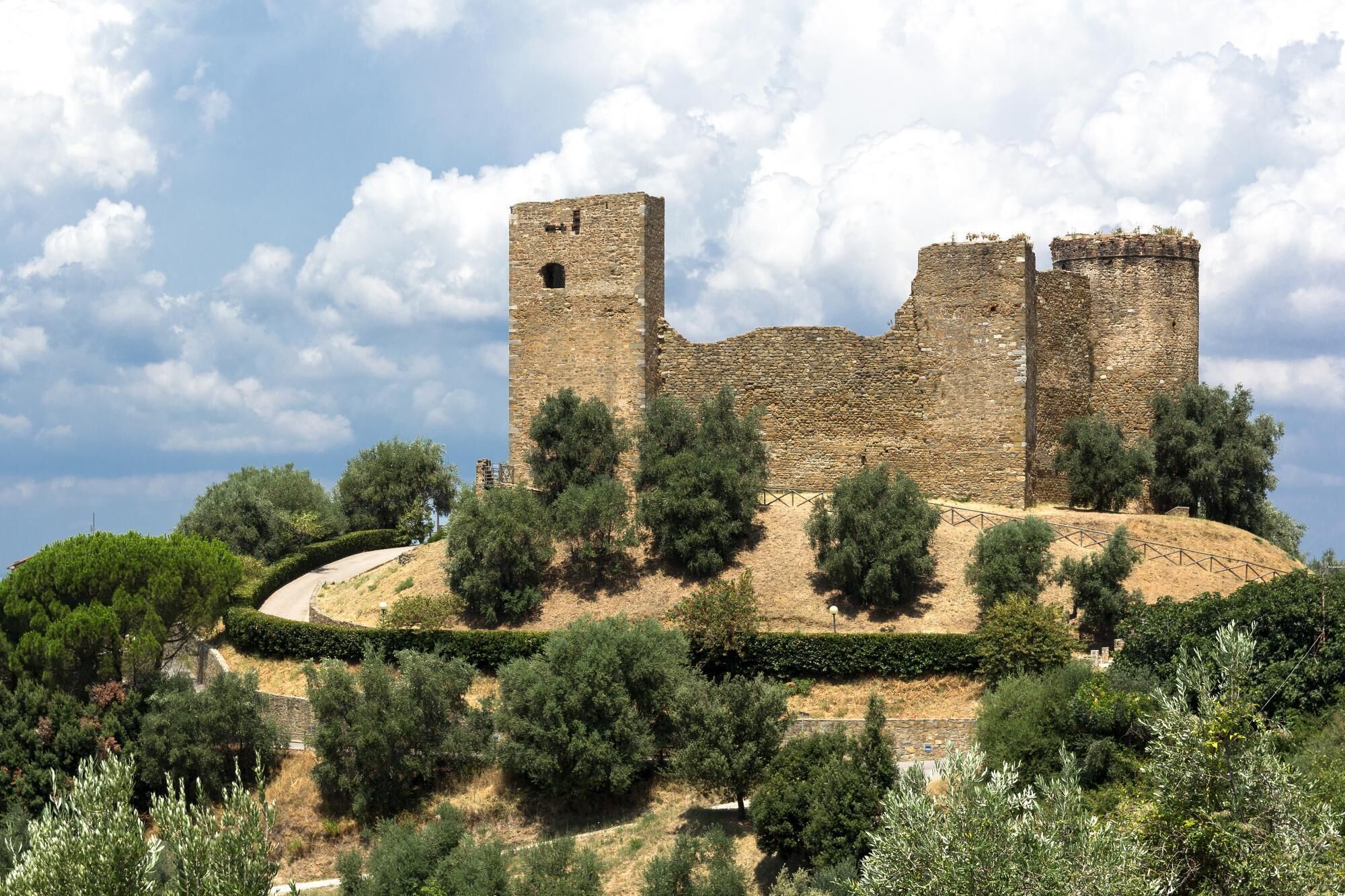 A historic stone castle with multiple towers, surrounded by dense greenery and a clear sky.