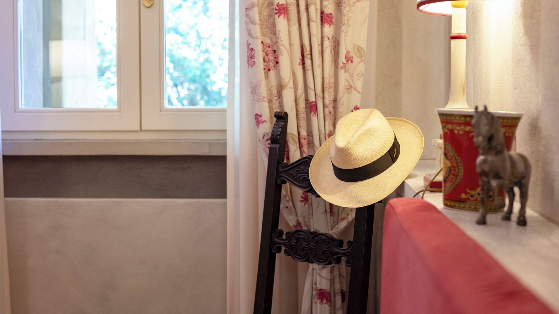 Une pièce avec une fenêtre, une chaise sur laquelle est posé un chapeau, une lampe et une statue de cheval décorative.