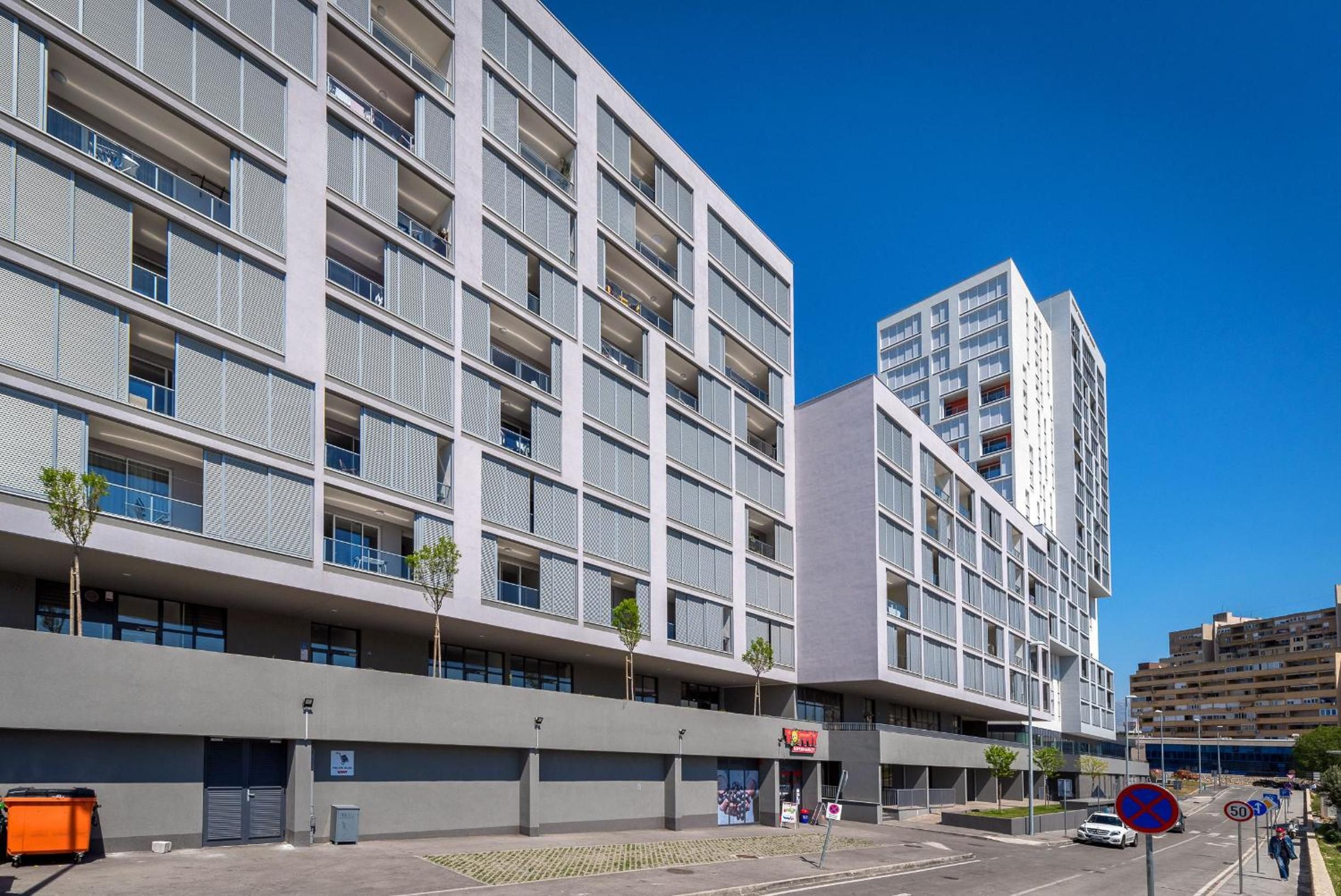 A multi-story building with balconies, a ground-level commercial area, and a clear blue sky.