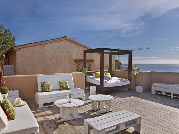 A rooftop terrace with white furniture, a wooden deck, and a view of the sea.