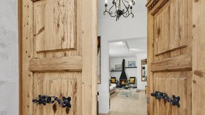 A wooden door with a metal handle, leading into a living room with a fireplace, a chandelier, and a sofa. - Villa Can Moya (Palma)