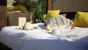 A bed with white bedding, two yellow pillows, a woven throw, a straw hat, a woven bag, and two glass tumblers. - Villa Can Moya (Palma)