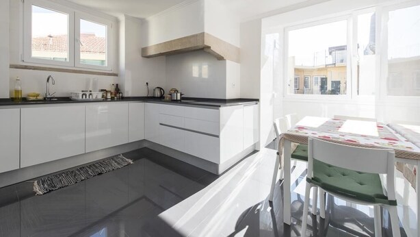 Una cocina moderna con armarios blancos, encimera negra y ventana con vistas a un barrio residencial.