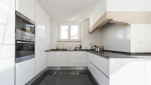 Una cocina moderna con armarios blancos, un horno de acero inoxidable y un ventanal sobre el lavamanos.