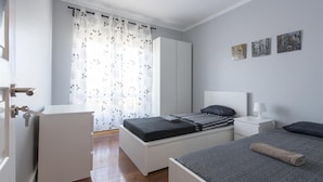 Un dormitorio con cama, mesitas de noche, armario y ventana con cortinas.