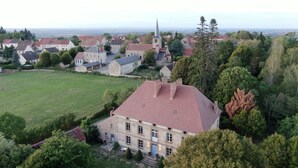 Une vue aérienne d’un village avec une église imposante et un grand bâtiment en pierre surmonté d’un toit rouge.