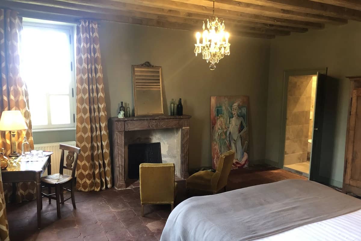 Una habitación con una cama, un escritorio con lámpara, una chimenea y un cuadro.