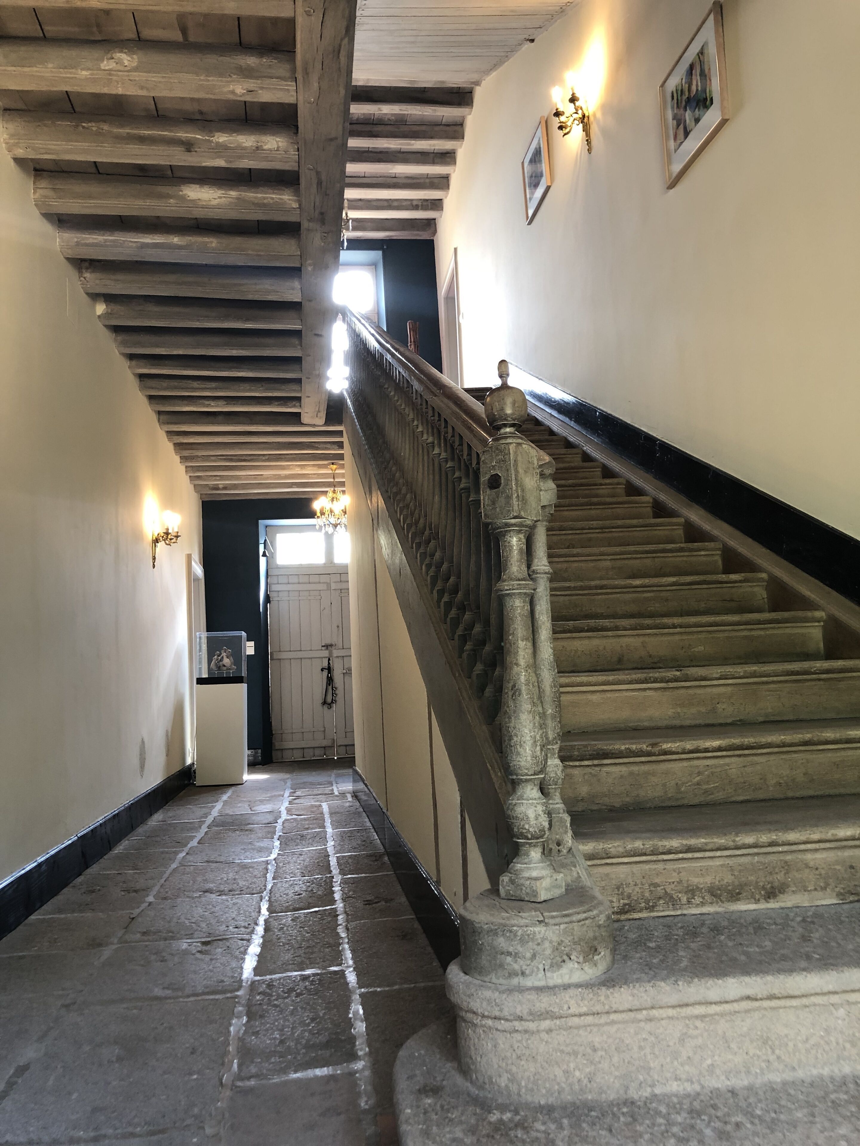 Een hal met stenen vloer die leidt naar een trap met een balustrade.