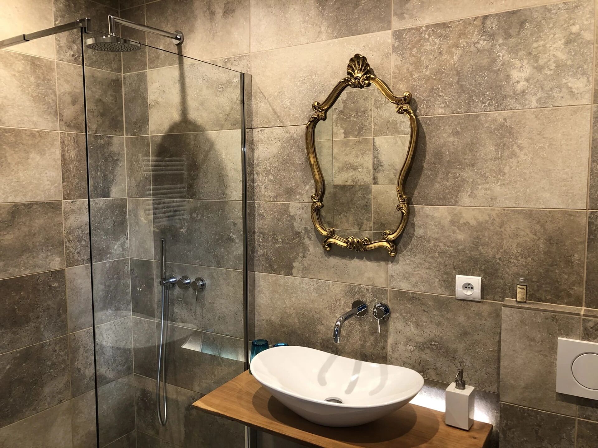 Un baño moderno con ducha de vidrio, un lavamanos blanco y un espejo con marco dorado.