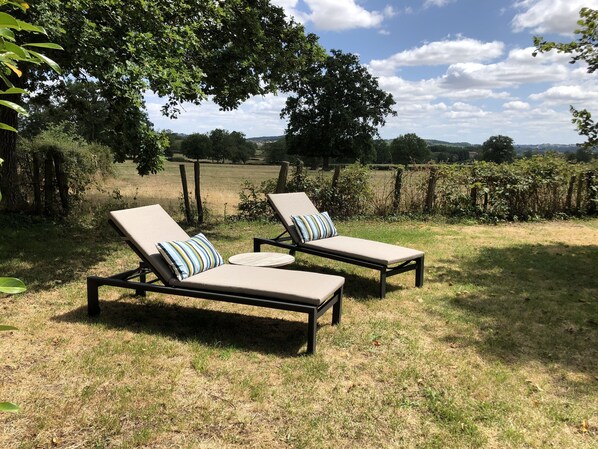 Two sun loungers with striped cushions in a grassy outdoor area with a view of a field and trees. - Zone Bleue (Hyds)