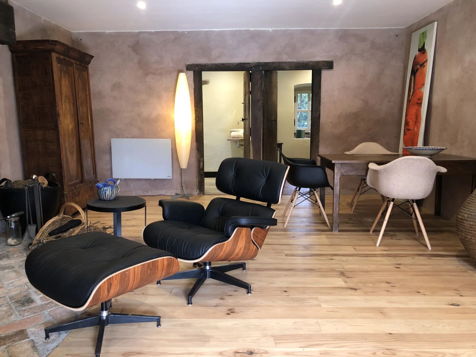 A modern interior with a wooden floor, a black leather sofa, a whiteboard, and a dining area with a table and chairs.