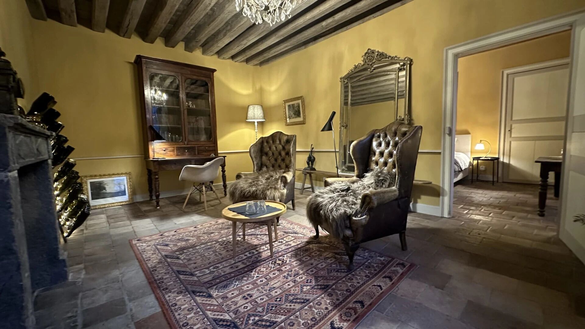 A room with a traditional design, featuring a large wooden cabinet, a tufted leather armchair, a patterned rug, and a chandelier.