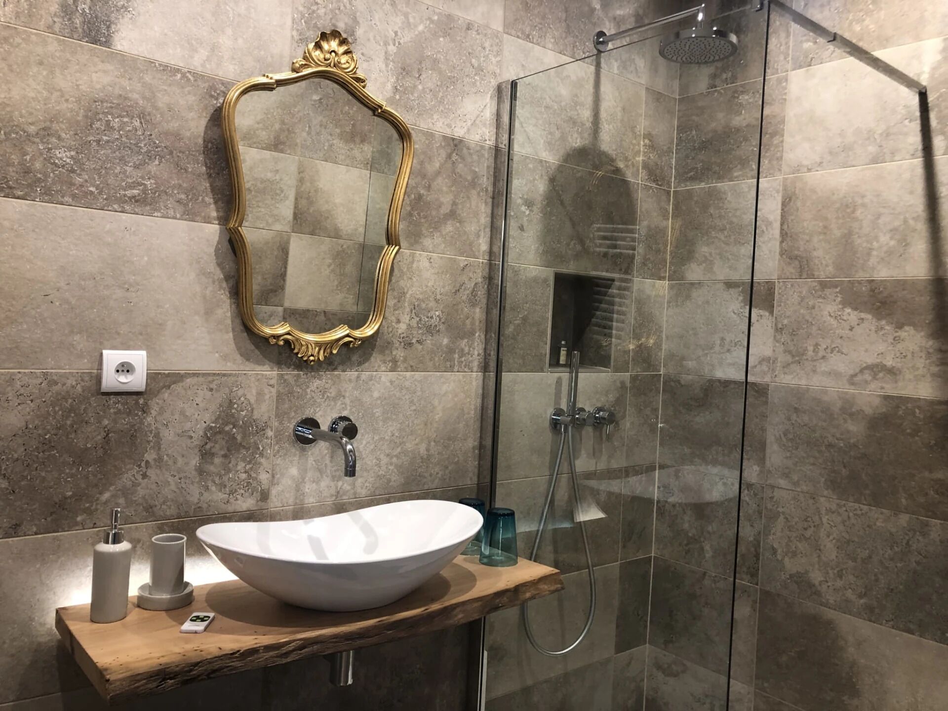 Un baño con un espejo grande, un lavamanos con lavabo blanco y una zona de ducha con mampara de vidrio.