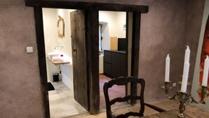 Un intérieur rustique avec une table et une chaise en bois, un chandelier et une porte-fenêtre donnant sur un espace cuisine.