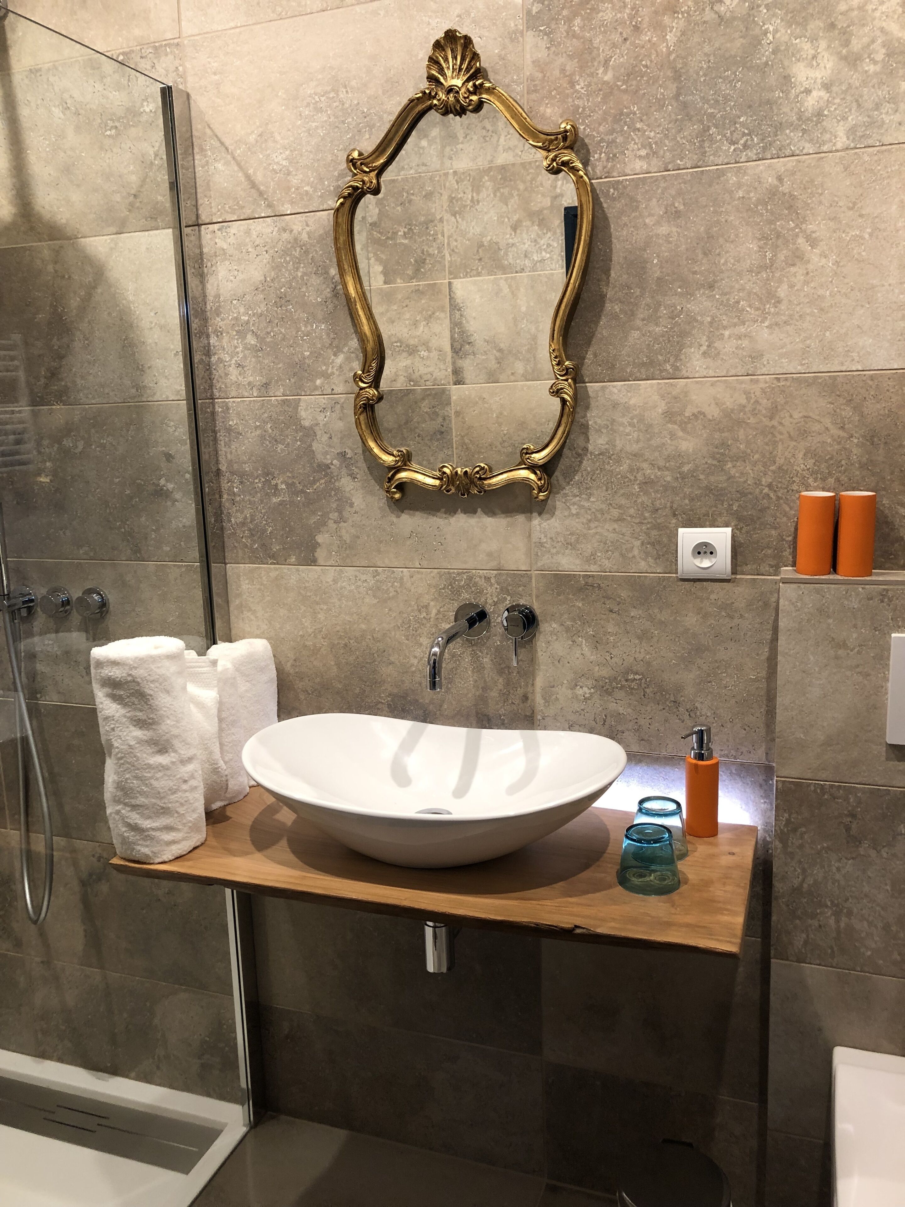 Un baño con un lavamanos blanco, espejo con marco dorado y dos dispensadores de jabón naranja.