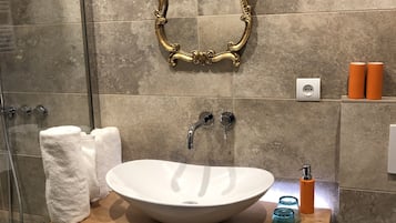 Un baño con un lavamanos blanco, espejo con marco dorado y dos dispensadores de jabón naranja.
