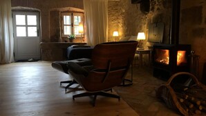 Un salon chaleureux avec un mur en pierre, une cheminée, un fauteuil confortable et un plancher en bois.