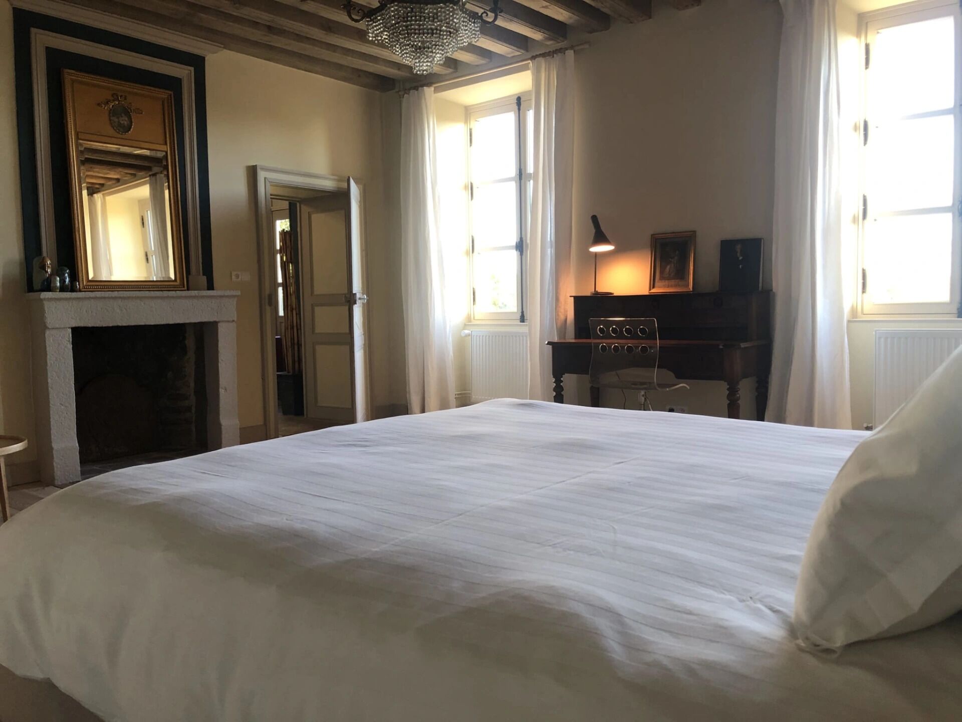 A hotel room with a large bed, a fireplace, a desk with a lamp, and a window with curtains.