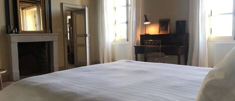 A hotel room with a large bed, a fireplace, a desk with a lamp, and a window with curtains.