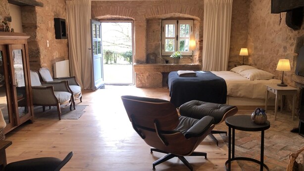 Une pièce confortable avec un lit, une chaise, une table et une cheminée.