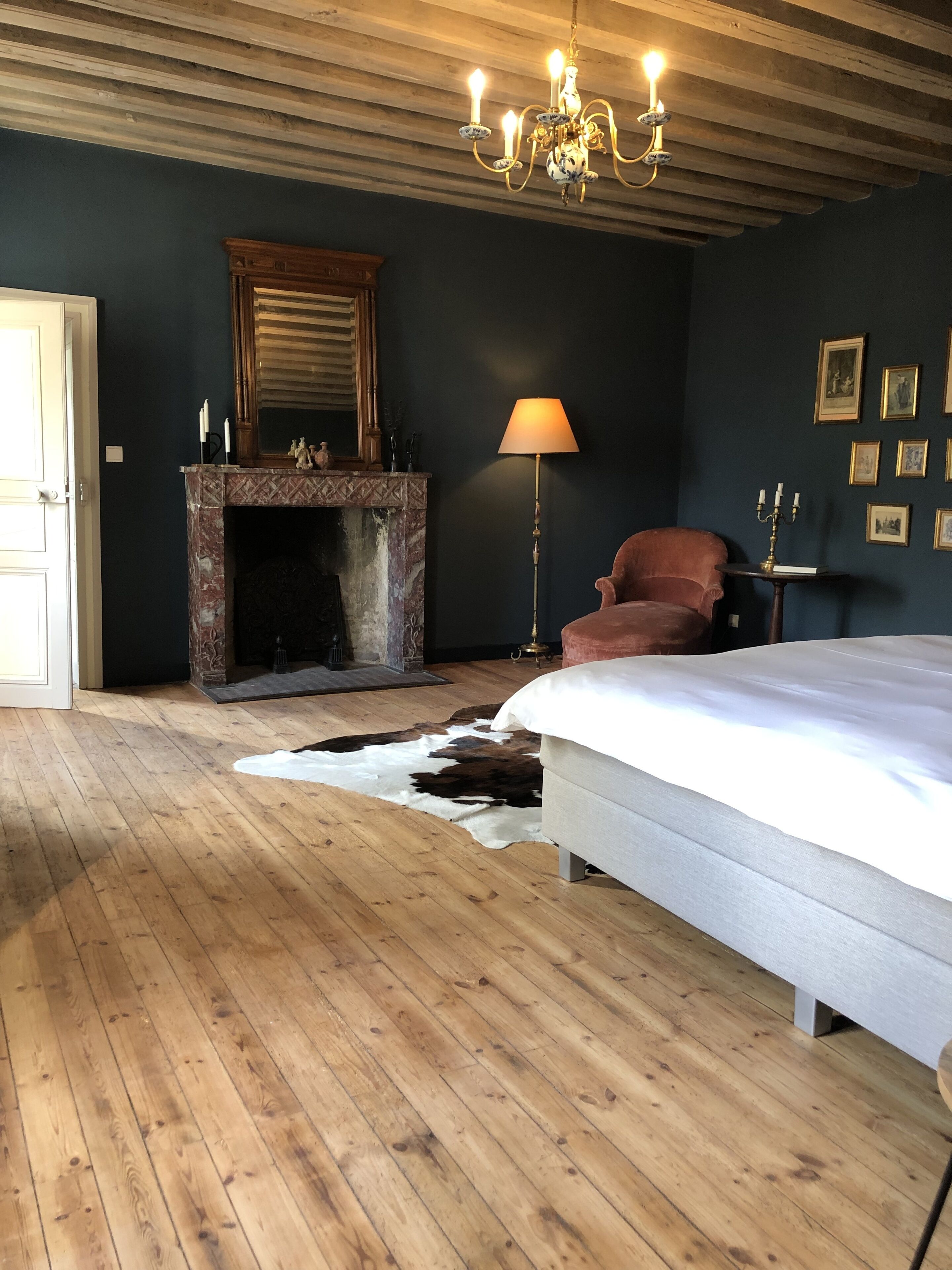 Ein Schlafzimmer mit Holzboden, einem großen Bett, einem Kamin, einer Chandelüster und einem Kuhfellteppich.