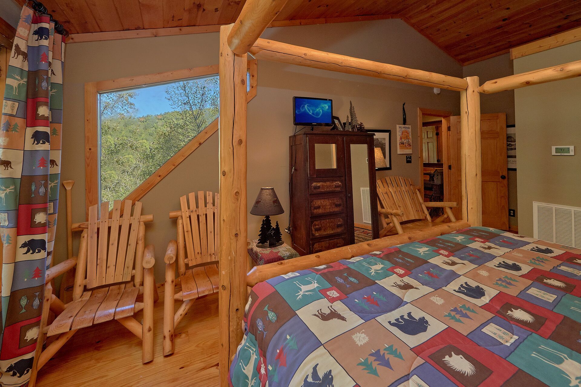 A rustic cabin bedroom with a wooden four-poster bed, a quilt with animal prints, a wooden rocking chair, a small cabinet, and a television on a wooden stand.