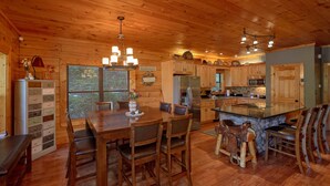 A wooden cabin interior with a dining area, kitchen, and bar seating. - Stonebrook Lodge: Firepit, Creekside, Theater Room (Sevierville)