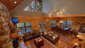 A spacious living area with a stone wall, a large wooden dining table, and a cozy fireplace. - Stonebrook Lodge: Firepit, Creekside, Theater Room (Sevierville)