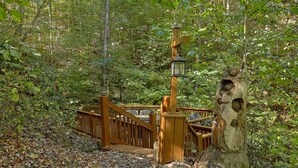 A wooden bridge leading to a wooden structure with a lantern and carved bear figures. - Stonebrook Lodge: Firepit, Creekside, Theater Room (Sevierville)