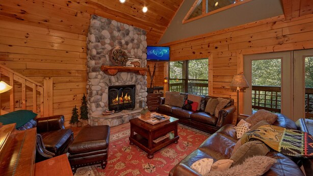 A cozy cabin interior with a stone fireplace, leather furniture, and a television. - Stonebrook Lodge: Firepit, Creekside, Theater Room (Sevierville)