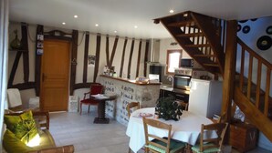 Une cuisine chaleureuse avec des poutres en bois, un coin repas avec une table et des chaises, et un escalier.