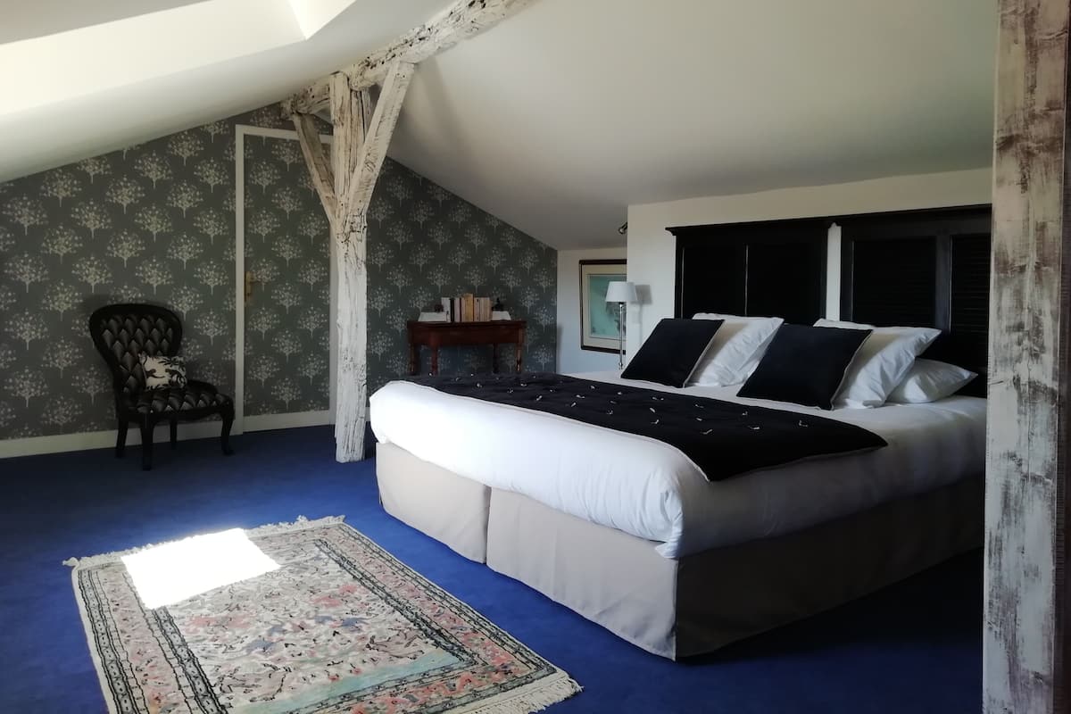 A bedroom with a bed, a chair, a small table, and a patterned rug.