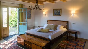 A bedroom with a large bed, wooden headboard, bedside tables, a chandelier, and a colorful rug. - B&B Clos de Saint-Maime (Saint-Maime-de-Pereyrol)