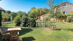 A rustic stone building with a garden patio, wooden furniture, and a wooden fence. - B&B Clos de Saint-Maime (Saint-Maime-de-Pereyrol)
