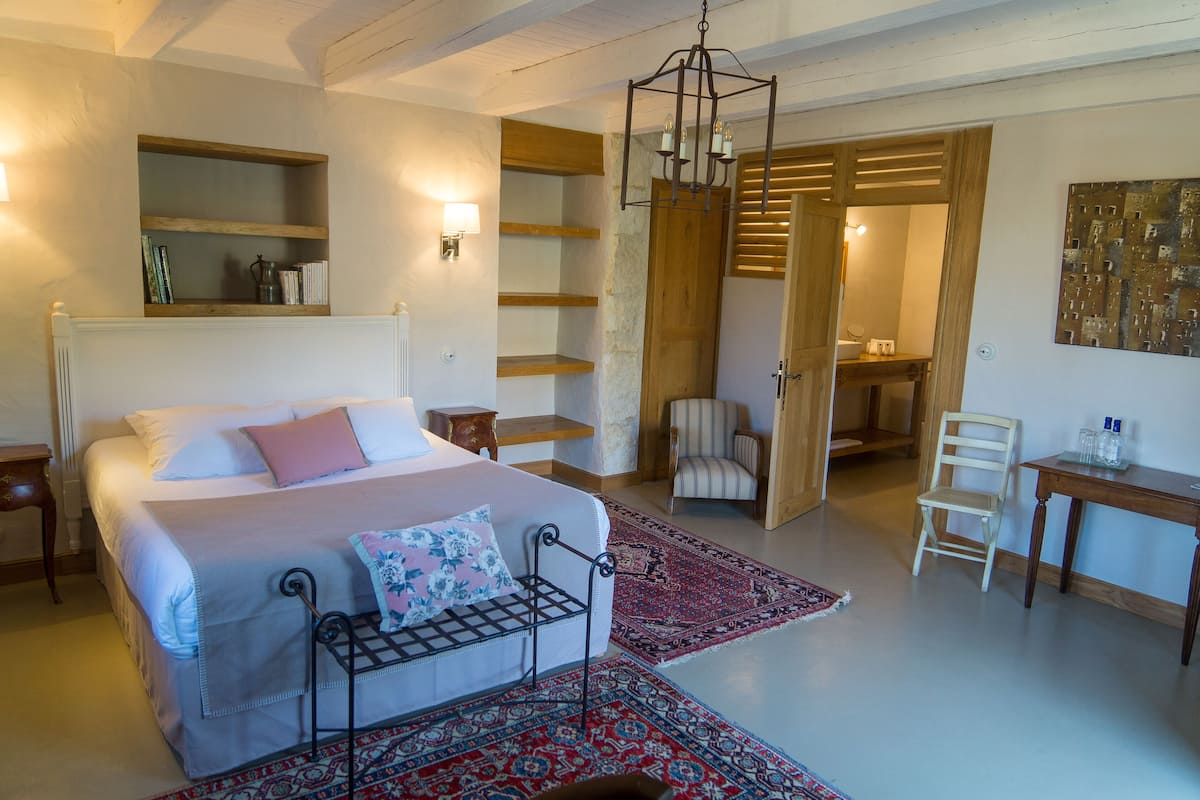 A bedroom with a bed, bedside tables, a chair, a desk, and a hanging light fixture.