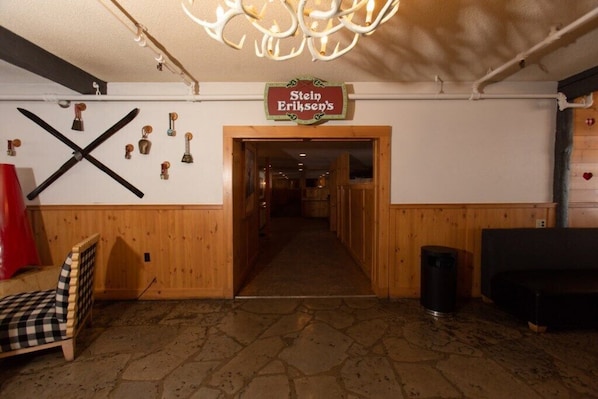 A hotel lobby with a wooden floor, a checkered chair, a sign for 'Stein Eriksen's,' and a chandelier.