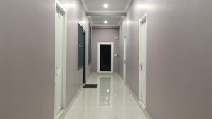 A hallway with white tiled floors and walls, featuring doors on both sides and a ceiling with recessed lighting. - The 1998 Homestay (Aizawl)