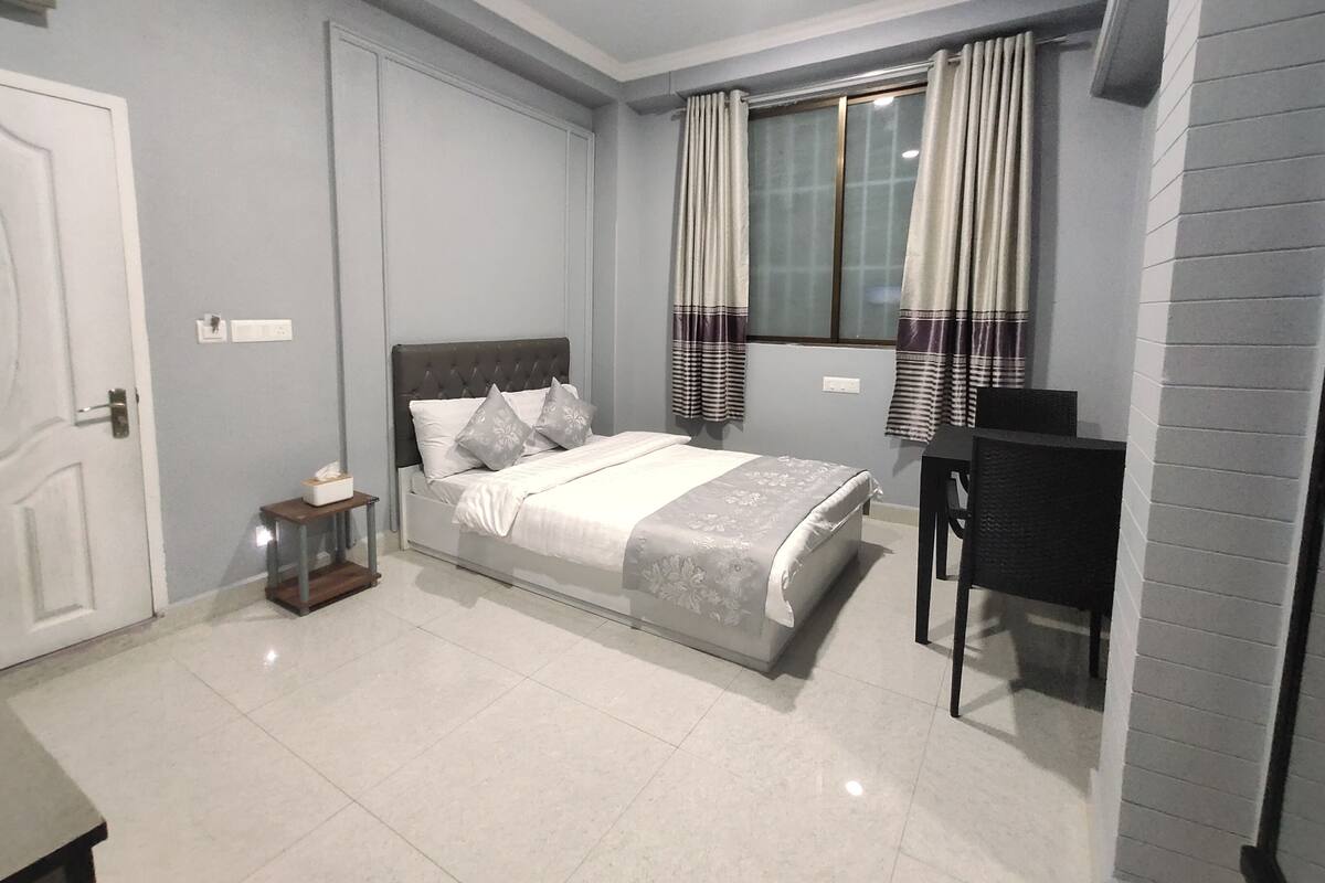A bedroom with a bed, a desk, and a window with curtains.