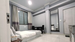 A compact hotel room with a bed, a small table, a chair, and a mirror. - The 1998 Homestay (Aizawl)