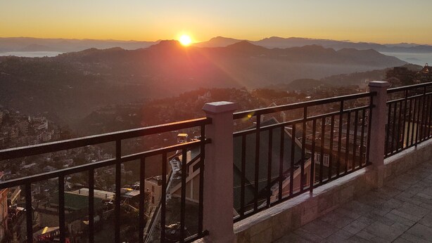 A balcony with a metal railing overlooking a cityscape during sunset. - The 1998 Homestay (Aizawl)
