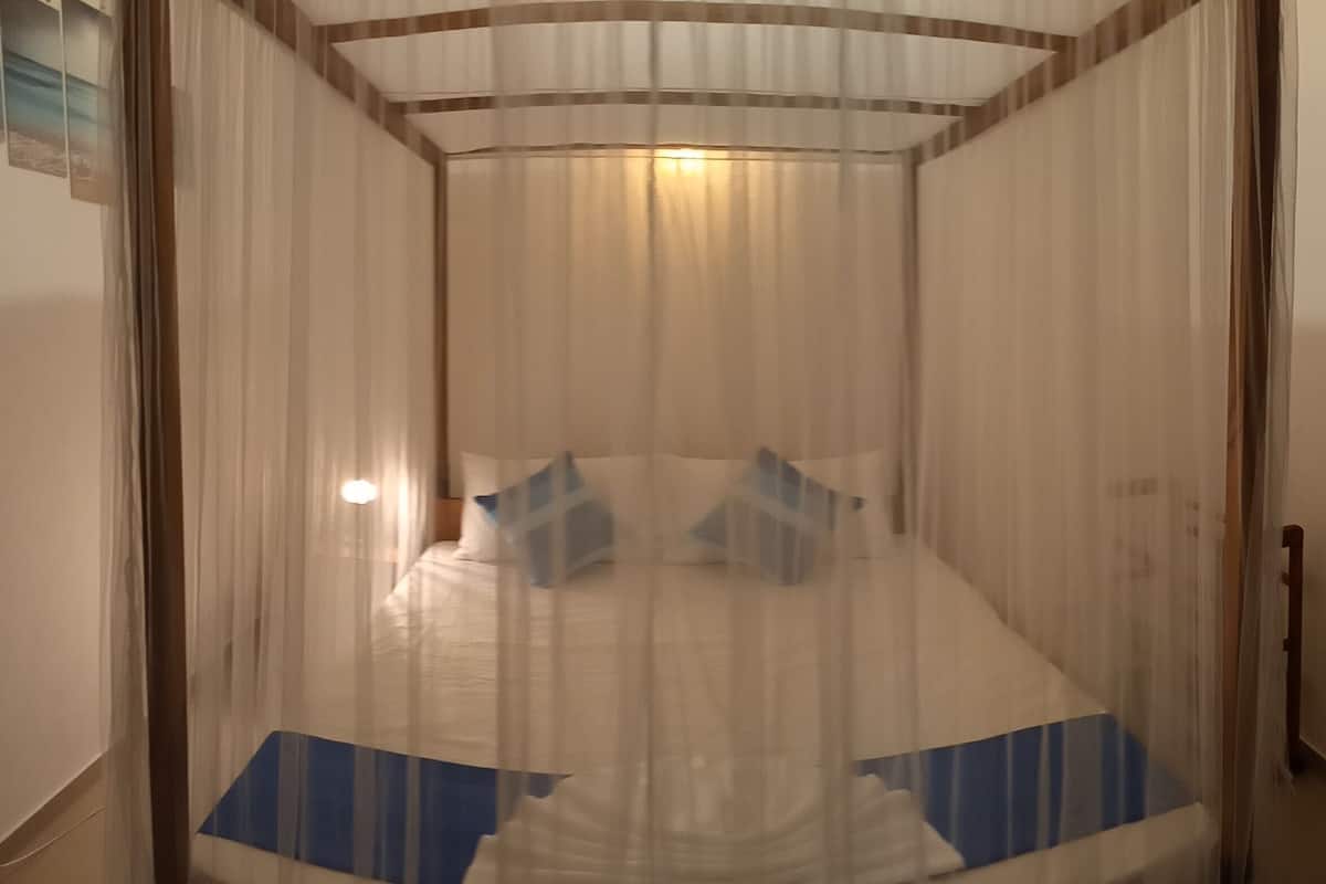 A room with a bed covered by a sheer curtain, a bedside table, and a wall-mounted light.