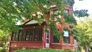 Un edificio in mattoni rossi con ampie finestre e una porta bianca, circondato da alberi verdi e rigogliosi.