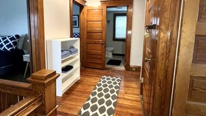 Un corridoio con pavimento in legno, un tappeto a motivi, un mobile contenitore bianco e una porta in legno.