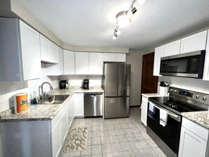 Una cocina moderna con armarios blancos, electrodomésticos de acero inoxidable, lavavajillas, refrigerador, microondas y horno.