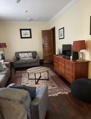 Una sala de estar con sofá, mesa de centro, aparador de madera y televisor.