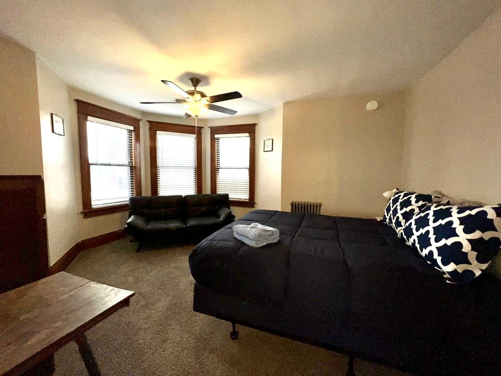 Une chambre à coucher avec un lit, un canapé, un ventilateur de plafond et de grandes fenêtres.
