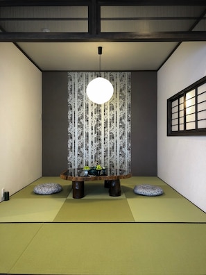 A traditional Japanese room with tatami flooring, a low table with a hanging light, and a shoji screen with bamboo patterns.